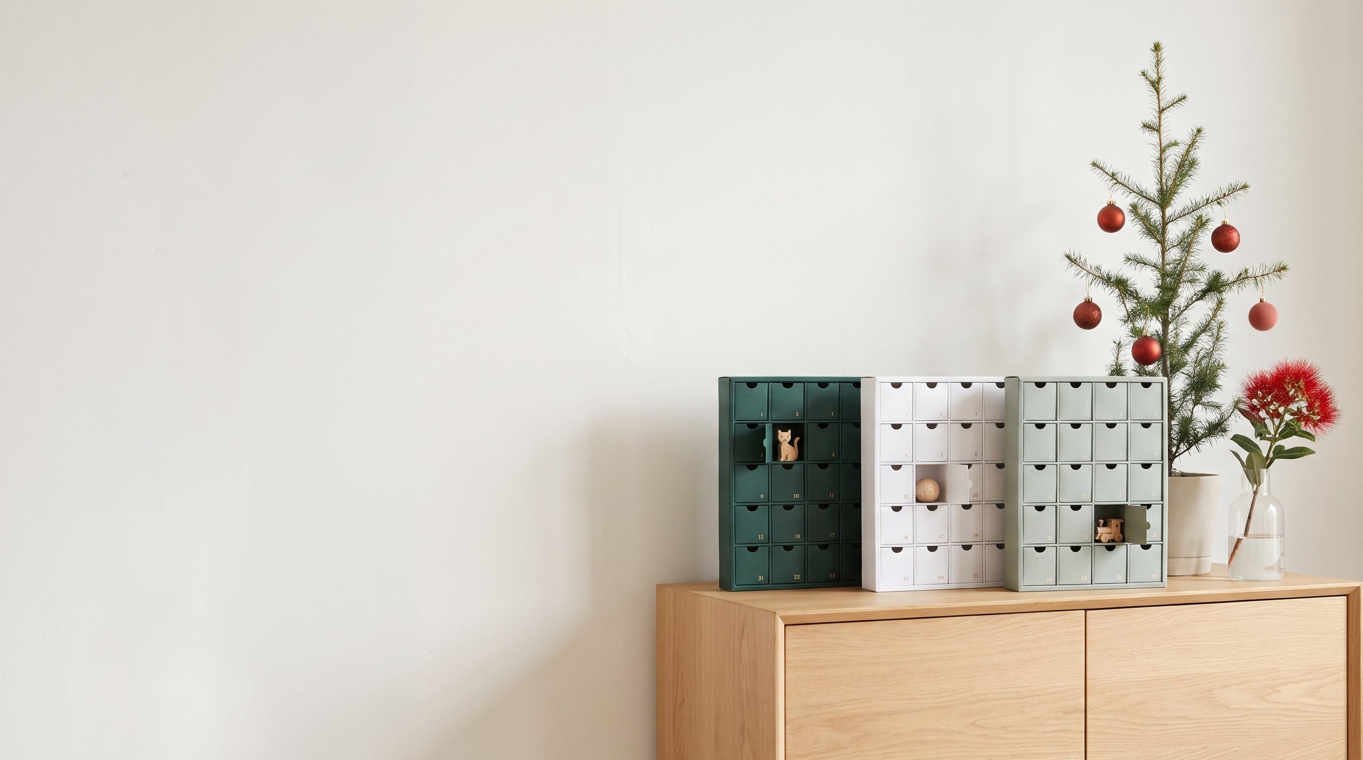 Advent calendars on an oak sideboard with a small Christmas tree and pohutukawa